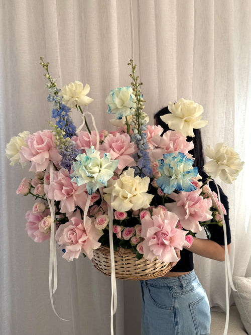 Pink, white and blue roses and delphiniums arranged in basket